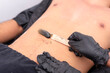 © Mdv Edwards - An esthetician applies hot black charcoal wax with a wooden spatula to a man's navel area during a hair removal procedure at a waxing salon.
