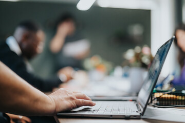 Blurred image of a business meeting in progress, highlighting a diverse team engaged in discussion with focus on a laptop in the foreground.