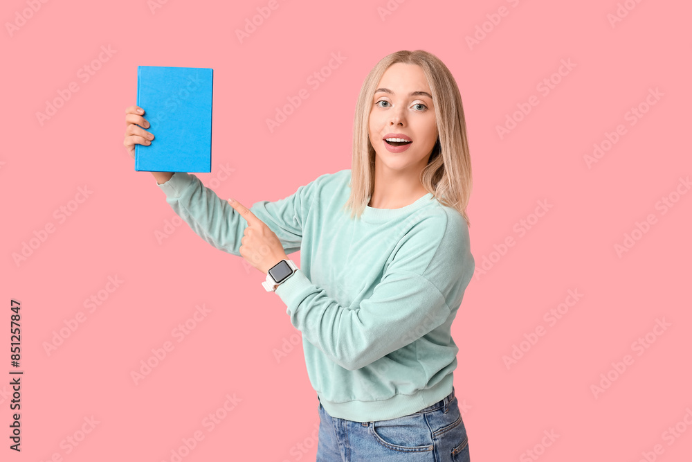 Beautiful young woman pointing at book on pink background