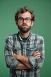 © Emanuel - Expressive portrait of a nerdy individual against a green background, conveying a sense of doubt, skepticism, or uncertainty through their facial expression and body language