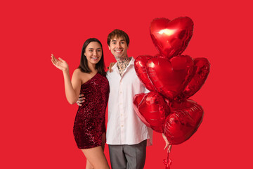 Wall Mural - Young couple with air balloons in shape of heart on red background. Valentine's Day celebration