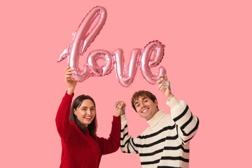 Wall Mural - Young couple with air balloon in shape of word LOVE on pink background. Valentine's Day celebration