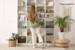 © Pixel-Shot - Young woman near shelving unit with clothes and decor at home