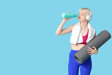 Wall Mural - Sporty young woman with yoga mat, towel and bottle of water on blue background