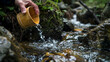 © Komkrit - A close-up of a figure drinking fresh water from a handmade bamboo cup, the crystal-clear stream running through a rocky forest area