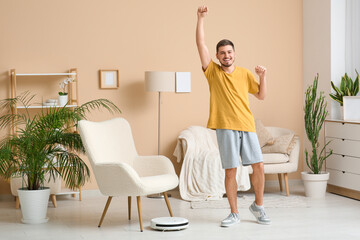 Sticker - Cheerful young man with modern robot vacuum cleaner at home