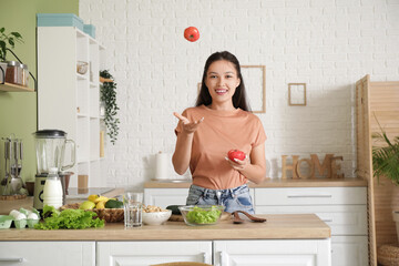 Poster - Beautiful young happy Asian woman with fresh tomatoes for salad in kitchen