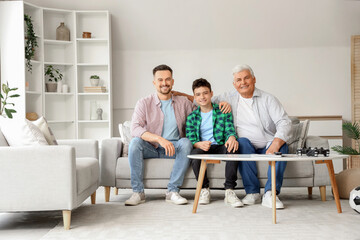 Wall Mural - Teenage boy with his dad and grandfather sitting on sofa at home