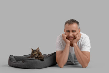 Wall Mural - Mature man with cute cat in pet bed on grey background