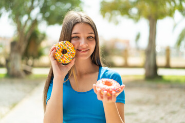 Wall Mural - Teenager girl at outdoors holding donuts with happy expression