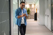 © Moon Safari - Positive male entrepreneur in glasses using social media apps over smart phone in office corridor