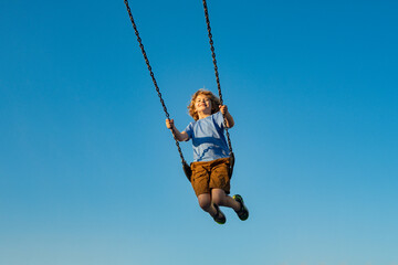 Wall Mural - Child extreme swinging. Danger high Swing in sky. Swing fly. Cute child having fun on a swing on summer sky background. Kids playing in park. Blonde little boy swings at kid playground.