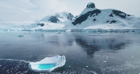 Wall Mural - Antarctica melting blue water iceberg. Antarctic ocean environment. Arctic ice glacier float polar ocean landscape, snow covered mountains in background. Cinematic ecology scene. Aerial drone flight