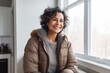 © CogniLens - Portrait of a satisfied indian woman in her 50s sporting a quilted insulated jacket in front of crisp minimalistic living room