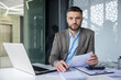 © Liubomir - Confident businessman working at his desk with a laptop in a modern office. Professional attire, serious expression, focused on paperwork.
