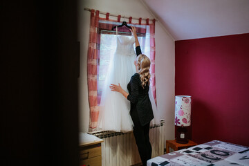 Wall Mural - A bride or bridesmaid carefully adjusts a wedding dress in an intimate, beautifully lit room, highlighting the delicate and meticulous preparations before the ceremony.