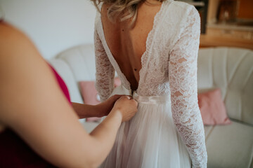 Wall Mural - A bride or bridesmaid carefully adjusts the laces or buttons of a wedding dress, highlighting the detailed preparations and anticipation before the ceremony.