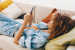 © SHOTPRIME STUDIO - A Happy Woman Relaxing on a Sofa, Holding a Mobile Phone and Smiling at the Online Game