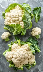 Fresh cauliflower heads arranged on a textured rustic surface with vibrant green leaves. The image highlights the natural beauty and freshness of the vegetables.