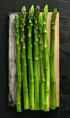 Poster - Fresh asparagus spears arranged on a cutting board against a black background. Suitable for culinary and cooking themes.