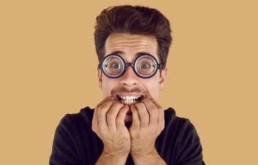 portrait of a funny stressed and nervous nerdy student. young man in round glasses biting his finger