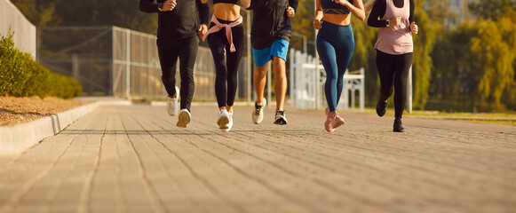 Legs of team of sporty people men and women running together in park having sport workout outdoors. Group of runners training in nature jogging in city. Healthy lifestyle and fitness concept. Banner.