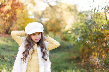 A smiling, stylish girl 5-6 years old in the autumn park. Happy childhood. Joyful and beautiful little girl.