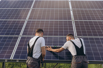 Two skilled workers or craftsmen wearing working gray uniforms, technicians are installing solar panels on a solar farm for clean energy and electricity supply