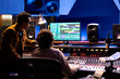 © DC Studio - Singer and producer work on soundboard controller at recording studio station. Sound engineer uses digital console for music production, operating on faders and key buttons at control desk.