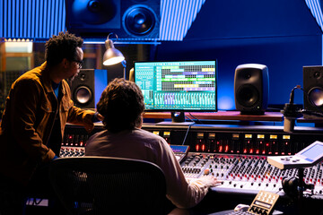 Fototapete - Singer and producer work on soundboard controller at recording studio station. Sound engineer uses digital console for music production, operating on faders and key buttons at control desk.