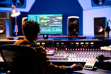 Poster - Music producer editing and processing sounds in control room with audio console and professional software on computer. Post production engineer uses motorized faders and twisting knobs.