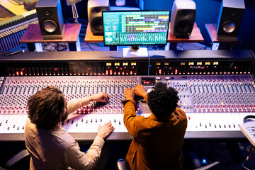 Fototapete - Musician and sound designer producing tunes on control panel board desk with daw software, professional recording studio. Team collaborating on hit songs, pressing buttons and sliders.