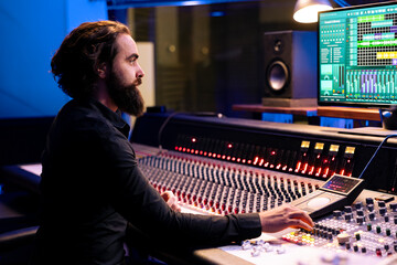 Fototapete - Tracking engineer editing new music with digital audio software and mixing console in control room, working in post production at studio. Audio technician operates sliders and knobs.