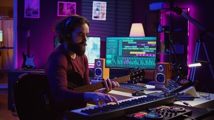 Fototapete - Musical composer recording his guitar tunes and adding piano key sounds, creating a beautiful song with mixing console and daw software. Sound engineer working with electronic tools. Camera B.