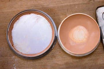 Used half empty makeup powder on the wooden table. Skin tone, pink color. Bronzer or highlighter in brown beige. Eyeshadow palette. Old and dirty sponge. Close up. Copy space. Selective focus.