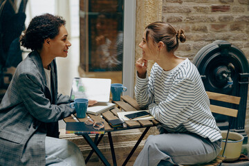 Wall Mural - Two young female colleagues working on new project while sitting at office terrace