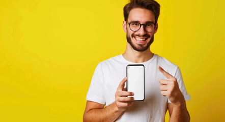 Wall Mural - Portrait of an excited man holding a large smartphone with a white blank screen and pointing at it, standing over a yellow background.