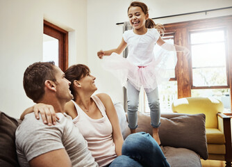 Canvas Print - House, parents and girl in lounge, jump and family with smile, weekend break and bonding together. Active, happy mother and father on sofa, childhood and kid with energy, cheerful and joy with fun