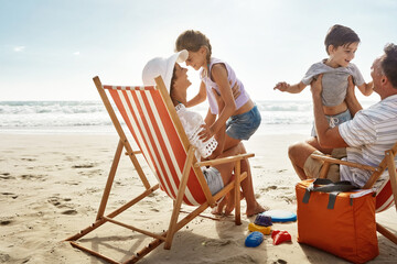 Canvas Print - Beach, sunshine and family with vacation, travel and excited with getaway trip, chairs and weekend break. Happiness, parents and kids with holiday, seaside and summer with freedom, playful and energy