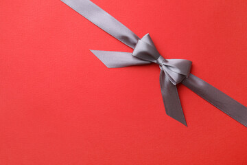 Wall Mural - Grey satin ribbon with bow on red background, top view. Space for text