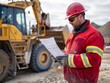 © ปรัชญา ตอพรม ตอพรม - A mining engineer wearing a hard hat and safety glasses reviews a document while standing in front of a large yellow bulldozer.
