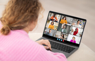 Poster - A woman is sitting at a desk and looking at a laptop screen. She is participating in a video conference call with eight other people. The people on the screen are in a grid layout