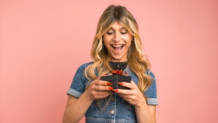 Wall Mural - Excited transgender woman opening small gift box against pink background