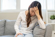 © KMPZZZ - Dizzy asian young woman, girl headache or migraine pain suffering from vertigo while sitting on couch in living room at home, holding head with hand, health problem of brain or inner ear not balance.
