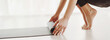 © Prostock-studio - A woman is seen rolling up her yoga mat on a clean, white floor in a bright and airy room. The atmosphere suggests a relaxing post-yoga session wrap-up, cropped, panorama with copy space