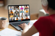 © Prostock-studio - A woman in a red shirt participates in a large online video conference meeting on her laptop. Her hands are on the trackpad, and she is looking at the screen with a focused expression.