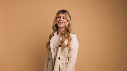 Wall Mural - Happy transgender woman in trench coat standing against beige background