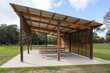 © Doublelee - A wooden gazebo or pavilion with a roof, featuring public bench seats, serves as a covered picnic area in a park, offering ventilation and recreational rest facilities.