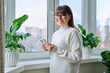 © Valerii Honcharuk - Smiling middle aged woman holding smartphone, at home near window