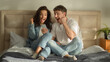 © Yuliia - Caucasian couple sitting on bed bedroom looking at screen smartphone mobile phone man woman enjoyment cellphone homeowner good news victory success achievement emotions celebrating surprise excitement
